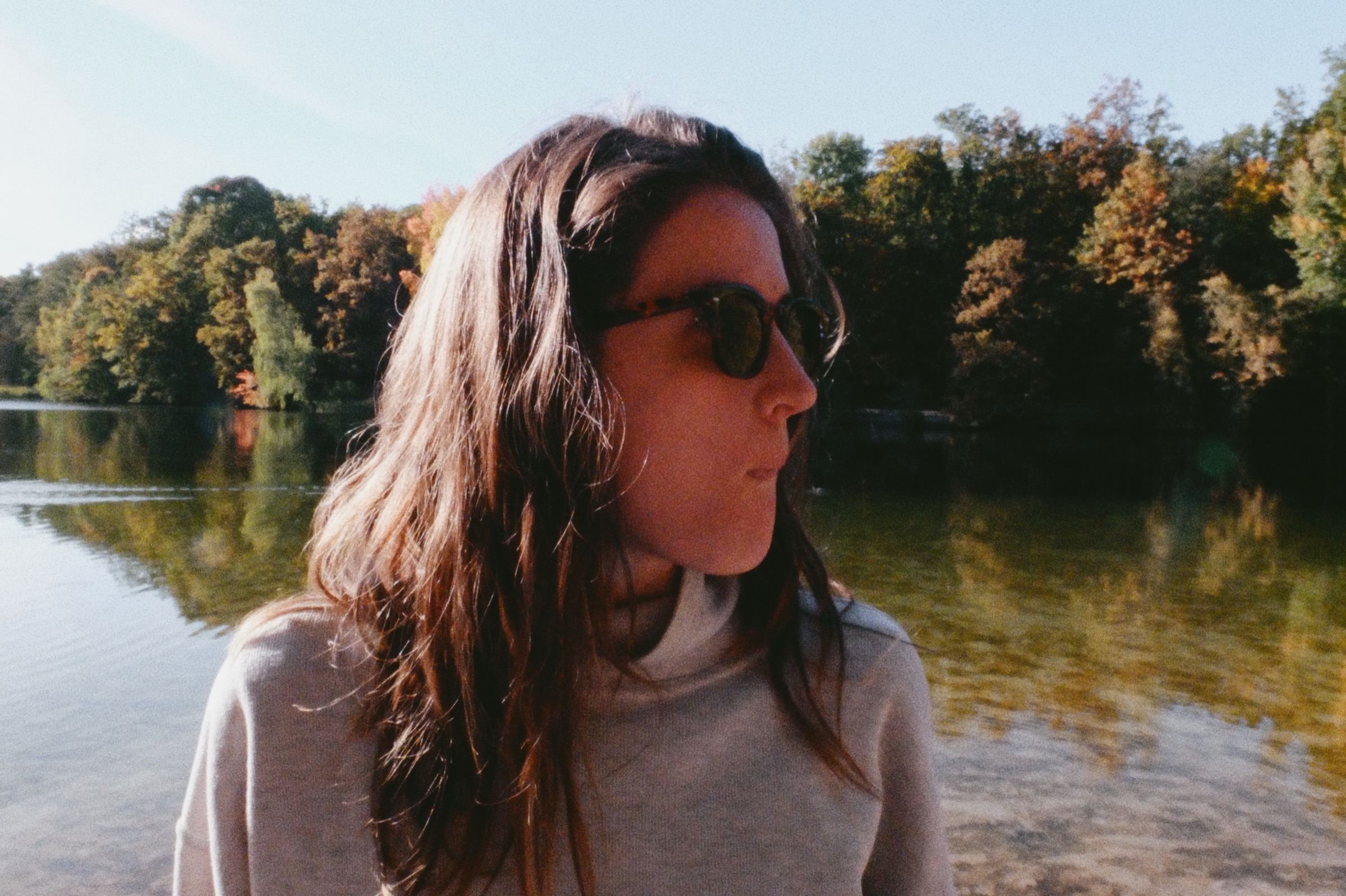 Mujer con anteojos de sol junto al lago, luz de otoño